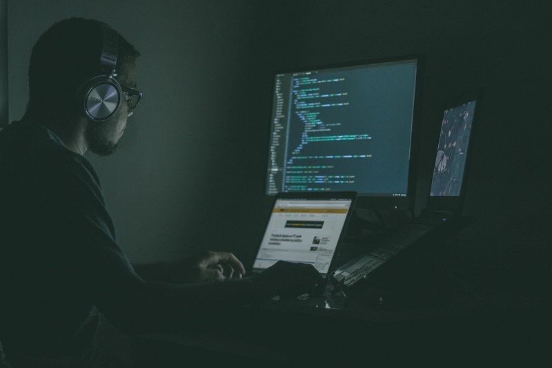 暗闇でパソコンに向かって作業する男　ネットでの詐欺のイメージ